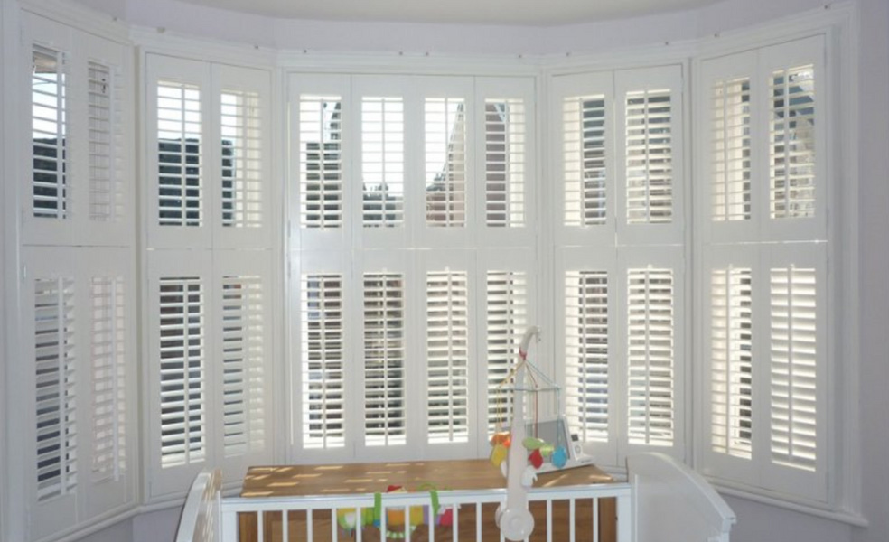 The image shows an interior view of a window with horizontal blinds partially closed, allowing natural light to enter the room.