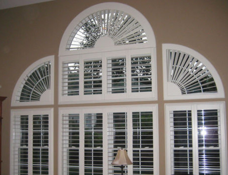 An interior view of a room with a large, arched window featuring shutters and a fan-shaped glass pattern.