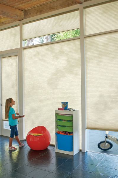 A person is standing in front of a window with vertical blinds that are partially open, allowing natural light to enter the room.