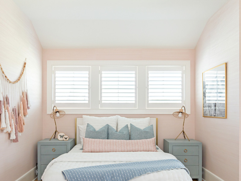 A spacious bedroom with a neatly made bed, two nightstands, a large window with white blinds, and a clean, modern aesthetic.